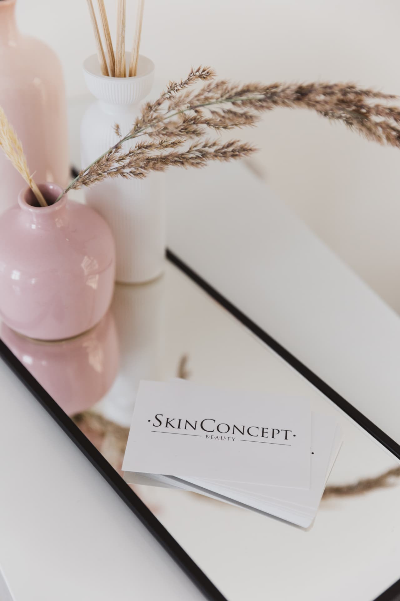 SkinConcept Beauty Visitenkarten auf einem Spiegeltablett mit Vasen und Trockengräsern